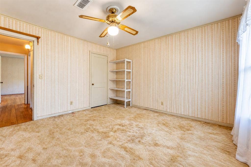 Room featuring textured carpeting, patterned wallpaper, built-in shelving, and a ceiling-mounted light fixture with integrated fan blades