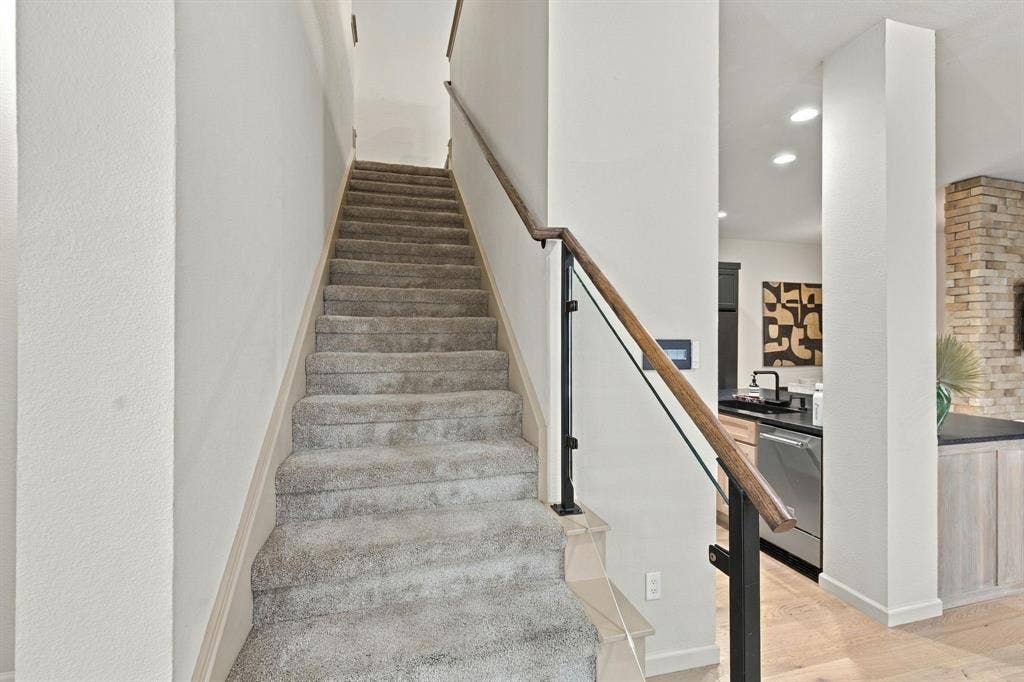 Staircase featuring wall-to-wall carpeting, wood-finish handrail, glass paneling, and black metal supports