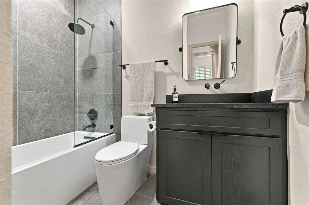 Bathroom featuring a dark vanity with a stone countertop, a glass-enclosed shower with matte black fixtures, and a wall-mounted mirror