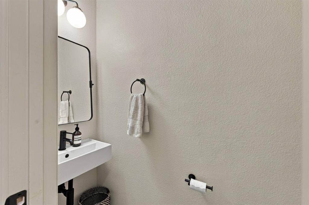 Wall-mounted rectangular sink with a matte black faucet, rounded rectangular mirror, and matching matte black hardware