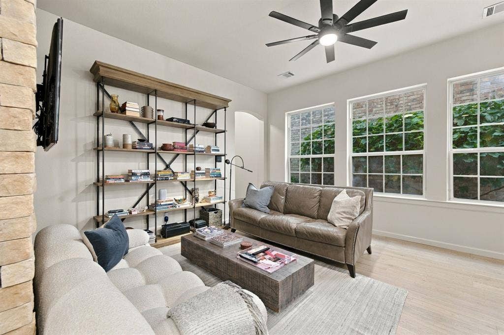Built-in metal and wood shelving unit, stone-accented wall, wood-finish flooring, and multi-pane windows with a modern ceiling fan