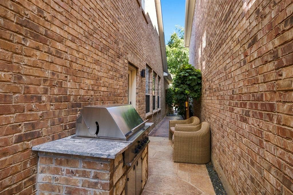 Side patio featuring a built-in stainless steel grill, natural stone countertop, brick exterior walls, and flagstone paving