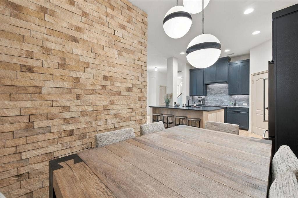 Textured stone accent wall, spherical modern pendant lighting, kitchen featuring dark cabinetry, stone-surface countertops, and a central island with wood-finish base cabinetry
