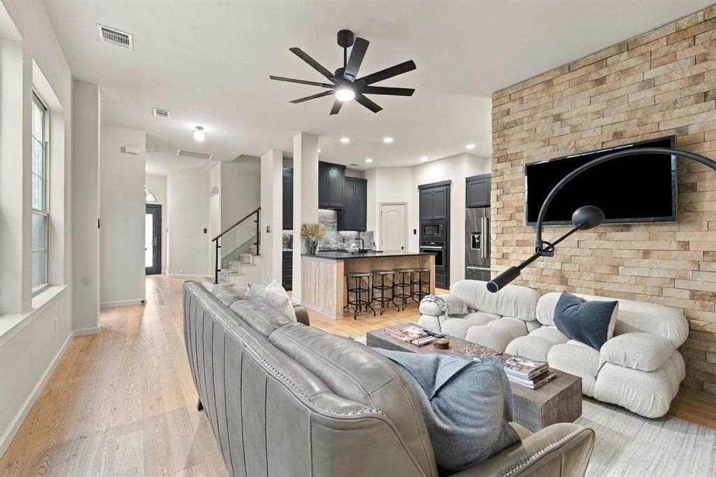 Stacked stone accent wall, wood-finish flooring, recessed lighting, multi-blade ceiling fan, and central kitchen island with built-in cabinetry