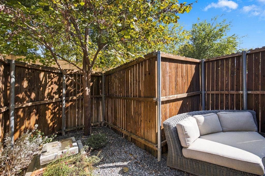 Outdoor space featuring wood-plank privacy fencing, metal support posts, a mature tree, and crushed stone ground cover
