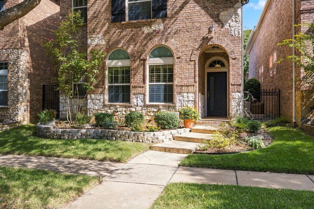 Brick and stone veneer facade featuring arched windows with muntins, a covered arched entryway, and stone-retaining garden beds