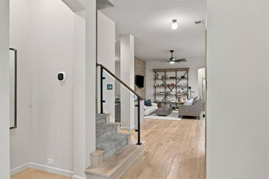 Interior space featuring wood-finish flooring, a staircase with a glass panel railing and dark metal accents, a textured stone accent wall, and a ceiling fan with integrated lighting