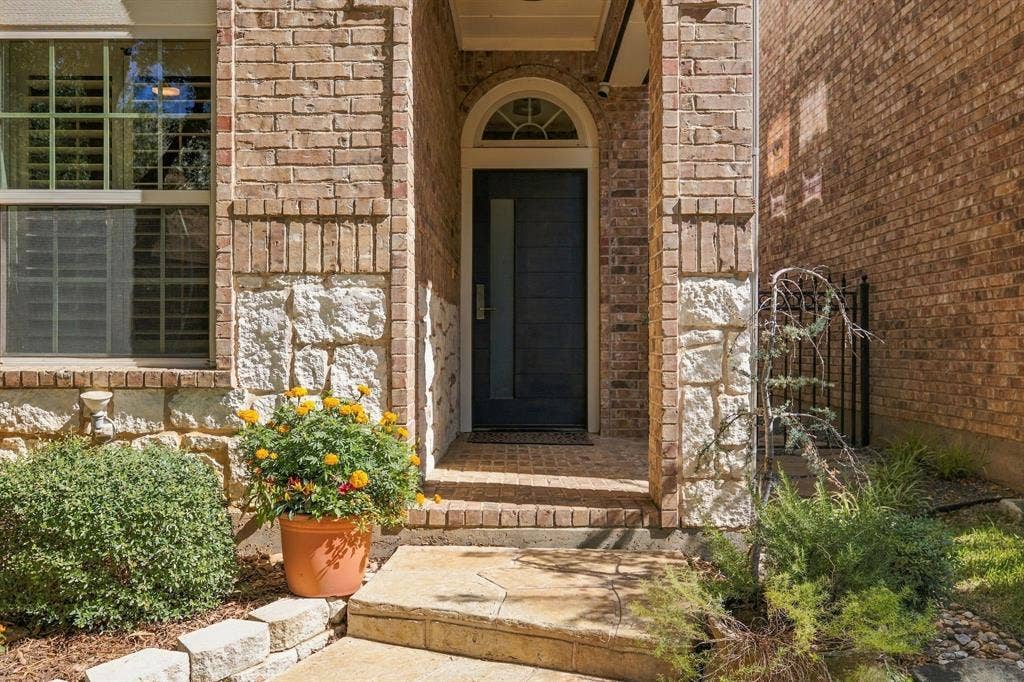 Exterior entryway featuring a brick and stone facade, arched transom window, covered porch, and a solid-panel entry door with vertical glass accent