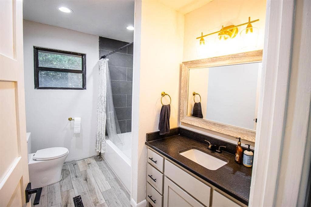 1040 Wedgewood Drive, Woodway, TX 76712 Bathroom featuring a vanity with dark solid-surface countertop, rectangular undermount sink, wood-finish flooring, recessed lighting, and a bathtub with dark tile surround