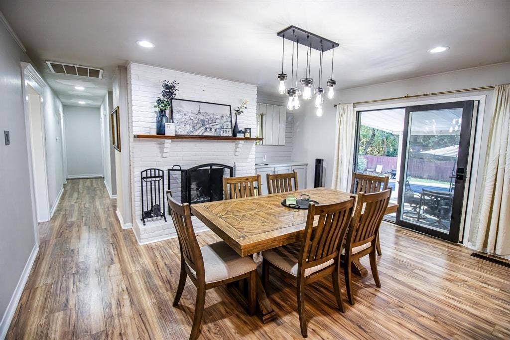 1040 Wedgewood Drive, Woodway, TX 76712 Dining area featuring wood-finish flooring, a painted brick fireplace with a wood mantel, a multi-pendant industrial-style light fixture, built-in cabinetry, and sliding glass doors