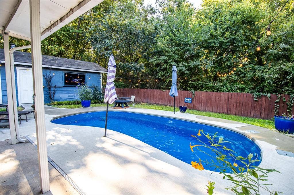 1040 Wedgewood Drive, Woodway, TX 76712 Curved in-ground swimming pool featuring a concrete deck and wood-style privacy fencing surrounded by mature trees