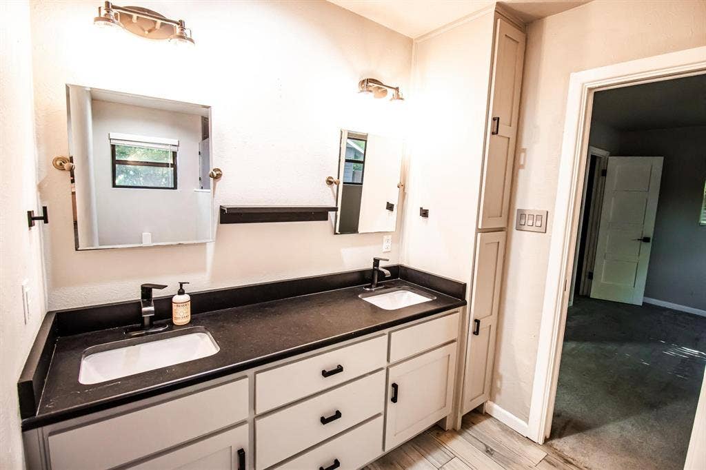 1040 Wedgewood Drive, Woodway, TX 76712 Dual-sink vanity featuring a dark countertop, white shaker-style cabinetry, matte black hardware, and integrated floor-to-ceiling cabinetry