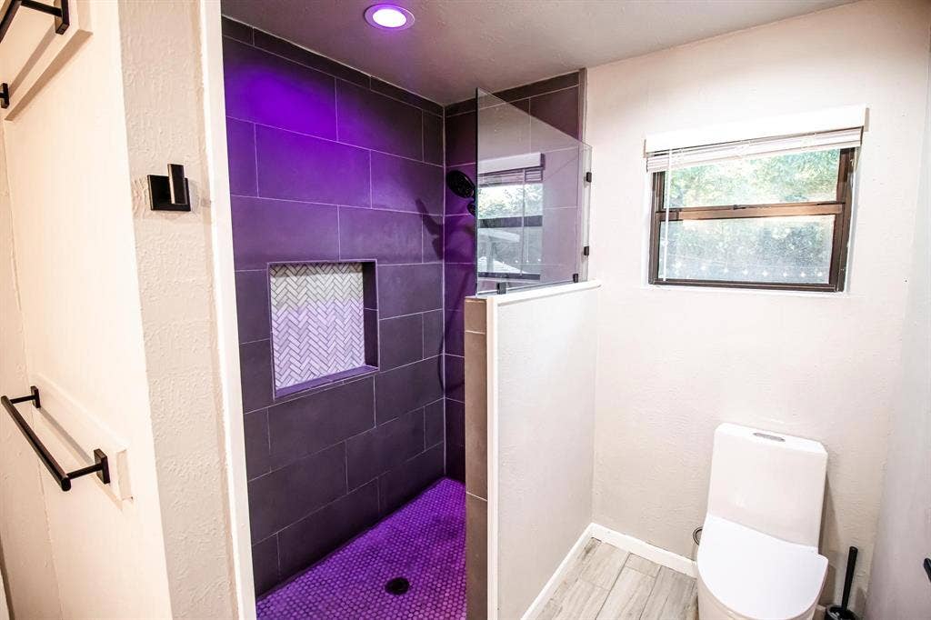 1040 Wedgewood Drive, Woodway, TX 76712 Walk-in shower featuring large-format dark tile, integrated herringbone-patterned wall niche, frameless glass panel, and matte black fixtures, complemented by wood-finish flooring