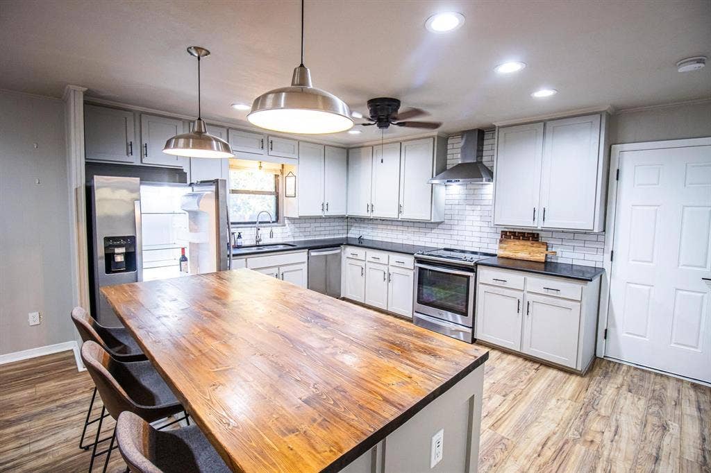 1040 Wedgewood Drive, Woodway, TX 76712 Kitchen featuring a central island with a butcher block countertop, white shaker-style cabinetry, stainless steel appliances, subway tile backsplash, and wood-finish flooring