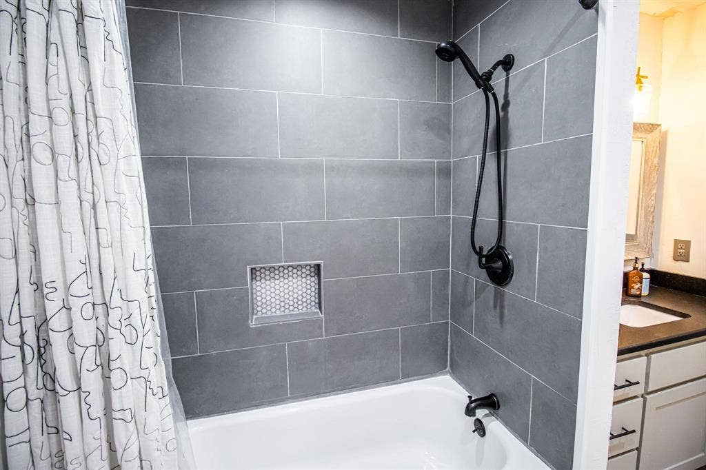 1040 Wedgewood Drive, Woodway, TX 76712 Shower area featuring large-format dark gray wall tile, a recessed hexagonal tile niche, and matte black plumbing fixtures