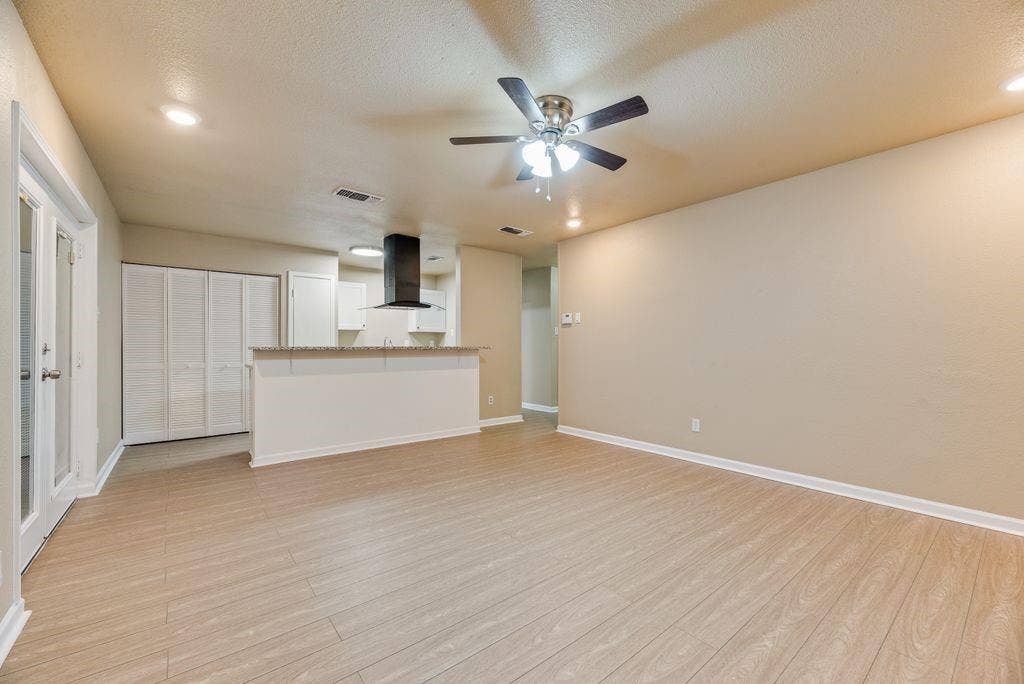 Open-concept space featuring wood-finish flooring, recessed lighting, a ceiling fan, a kitchen island with a stone countertop, and a modern black range hood