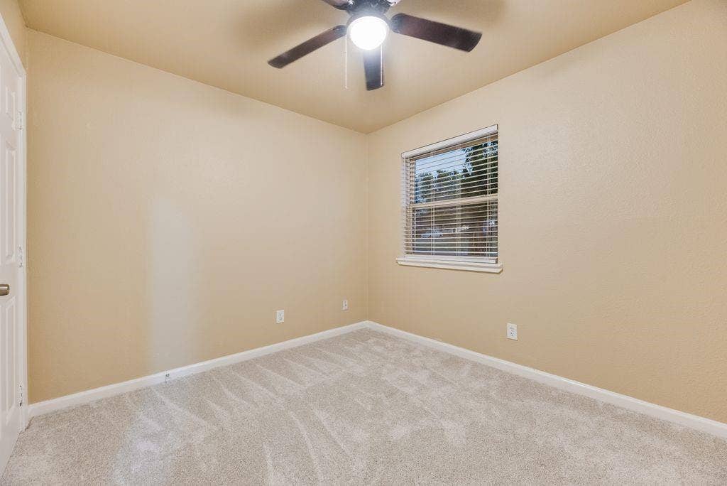 Neutral-toned interior featuring wall-to-wall carpeting, a multi-blade ceiling fan with integrated lighting, and a single-hung window with horizontal blinds