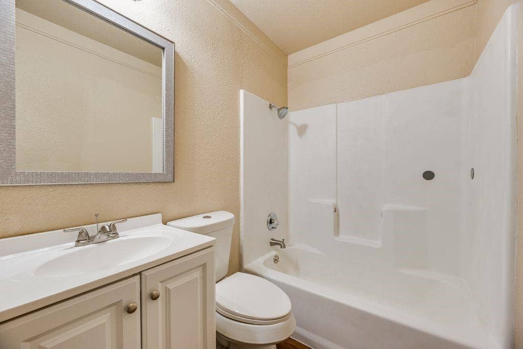 Bathroom featuring a white vanity cabinet with a integrated sink, polished metal faucet, wall-mounted framed mirror, and a white tub-shower combination with surround