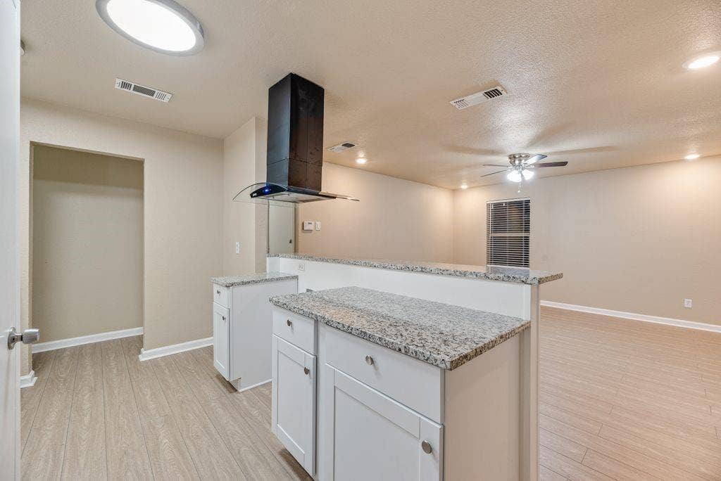 Kitchen featuring white shaker-style cabinetry, stone-finish countertops, stainless steel chimney-style range hood, and wood-finish flooring
