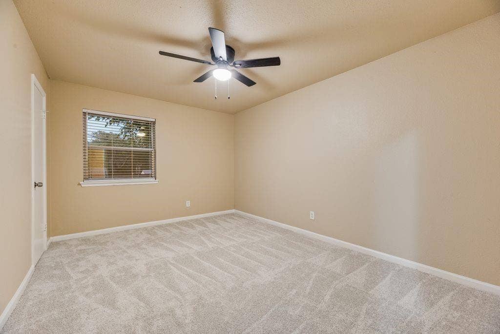 Neutral-toned walls, plush wall-to-wall carpeting, window with slatted blinds, and ceiling fan with integrated light fixture