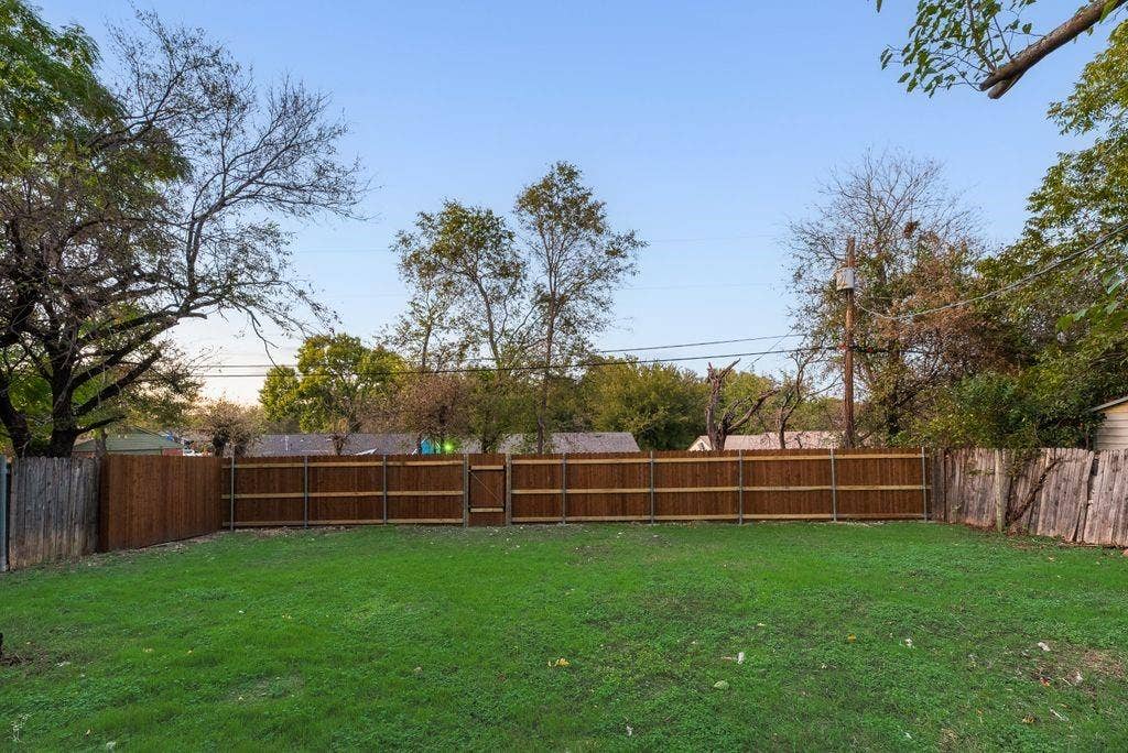 Private backyard featuring a level grass lawn, perimeter wood fencing, and mature trees