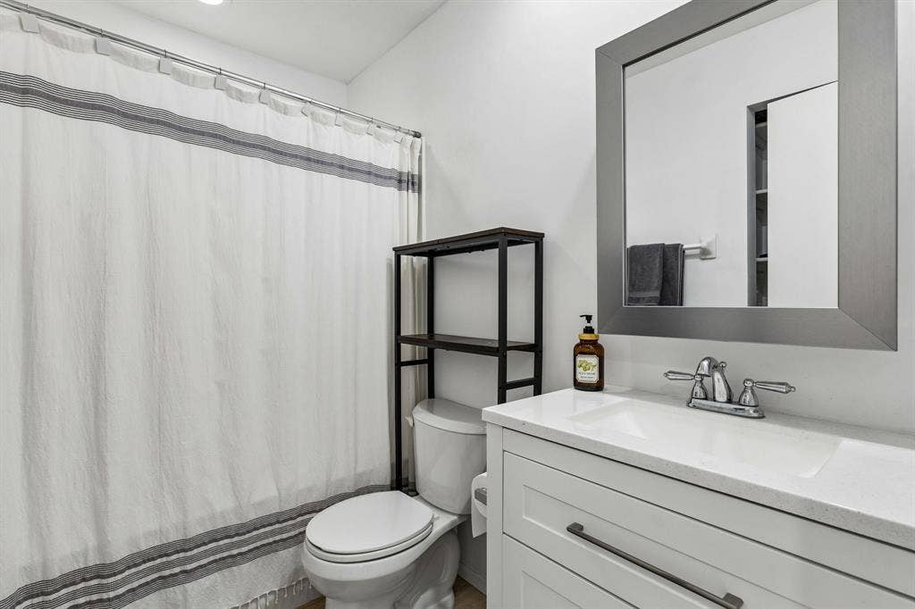 White vanity with a solid surface countertop, rectangular integrated sink, polished metal faucet, and framed rectangular mirror