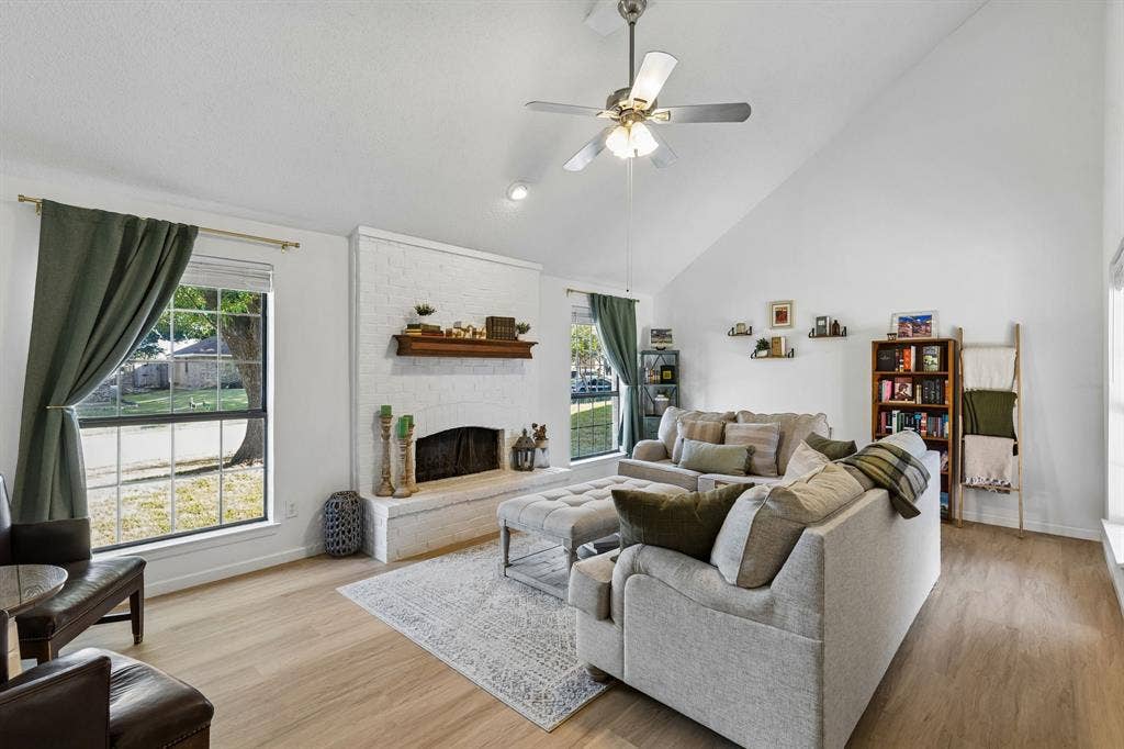 Vaulted ceiling, white-painted brick fireplace with a wood mantel, multi-pane windows, and light-toned wood-finish flooring