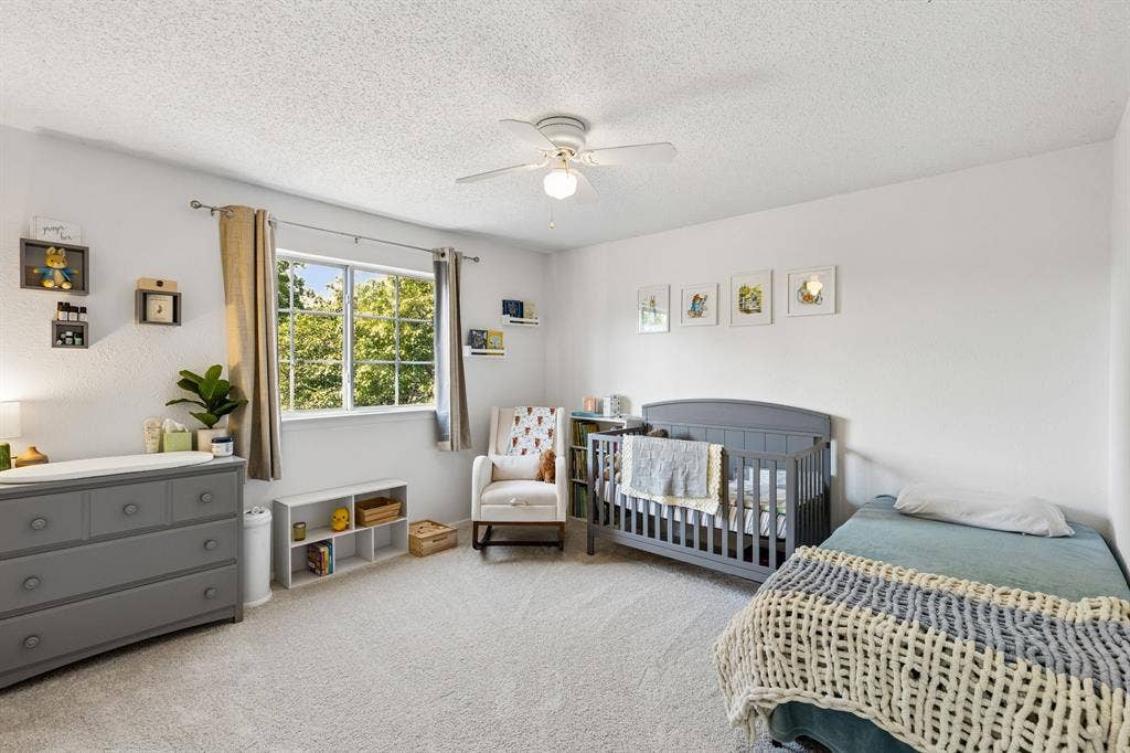 Neutral wall-to-wall carpeting, ceiling fan with integrated lighting, and a large window with window hardware