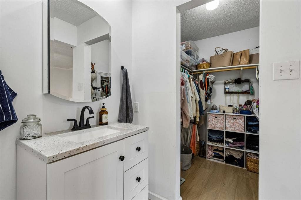 White vanity cabinet with a speckled surface, integrated rectangular sink, matte black faucet, and an arched wall-mounted mirror