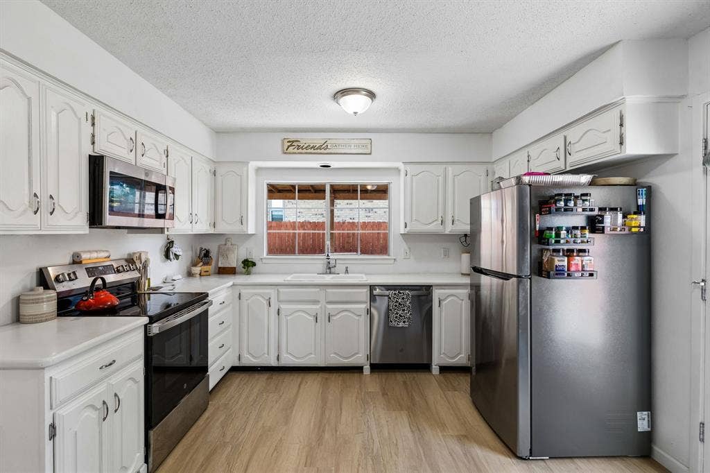 Kitchen featuring white raised-panel cabinetry, stainless steel appliances, a double-basin sink, and wood-finish flooring