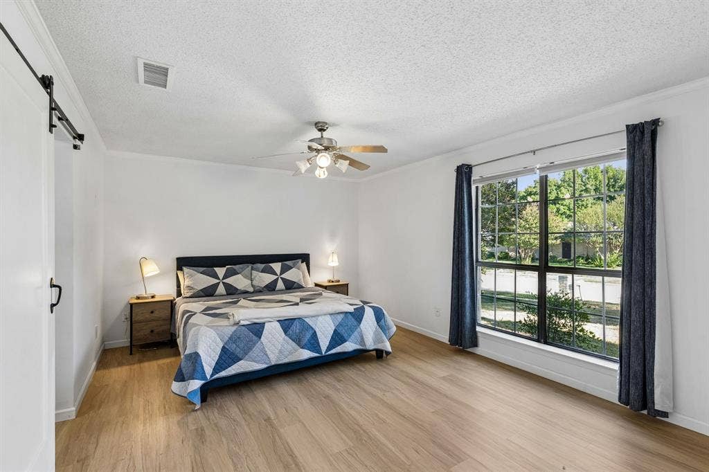 Bedroom featuring wood-finish flooring, a sliding barn door, a large multi-pane window, and a ceiling fan with integrated lighting