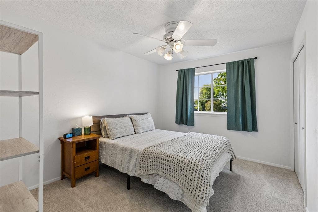 White-toned walls, ceiling-mounted multi-light fan, window with exterior grid, neutral carpeting, and a double-door closet