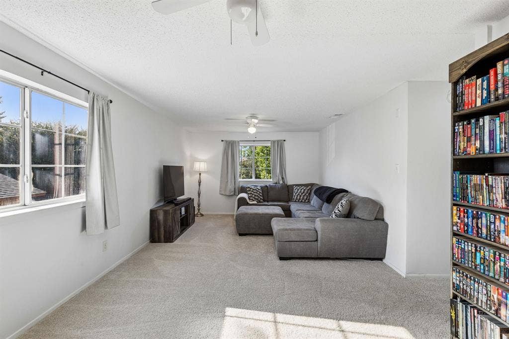 Living space featuring neutral carpeting, dual ceiling fans, and multiple windows providing natural light