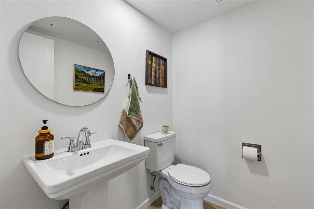 Pedestal sink with chrome dual-handle faucet, oval frameless wall mirror, and chrome toilet paper holder