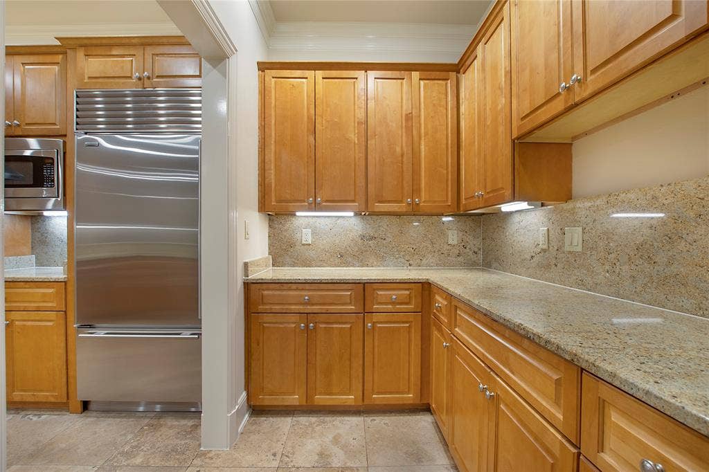 Kitchen featuring ornamental molding, built in appliances, light stone counters, and tasteful backsplash