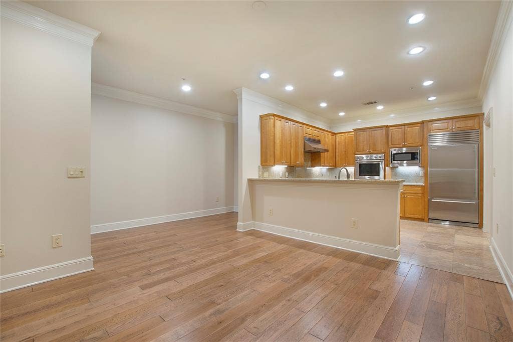 Kitchen featuring built in appliances, kitchen peninsula, ornamental molding, light hardwood / wood-style floors, and tasteful backsplash