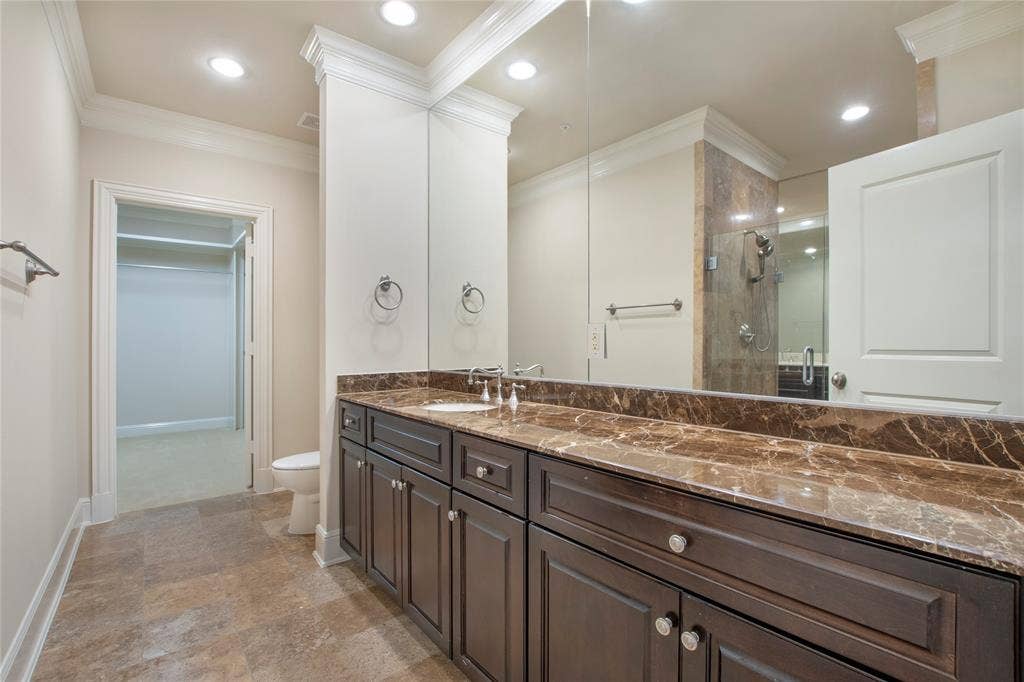 Bathroom featuring toilet, ornamental molding, a shower with shower door, and vanity