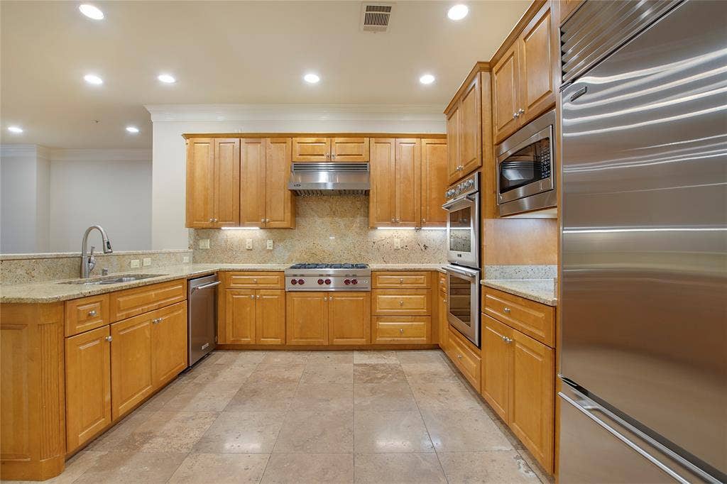 Kitchen with built in appliances, light stone countertops, sink, and decorative backsplash