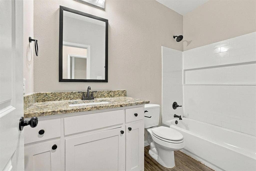 1116 S 6th Avenue, Denison, TX 75021 Bathroom featuring white shaker-style cabinetry, stone-finish countertop, undermount sink, matte black hardware, and a tub-shower combination with white subway-style wall tiling