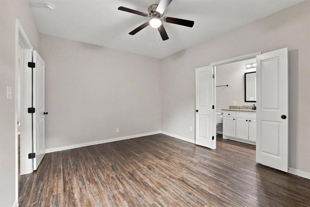 1116 S 6th Avenue, Denison, TX 75021 Neutral-toned room featuring wood-finish flooring, a central ceiling fan with integrated lighting, and double doors opening to an auxiliary space with a white vanity and stone-surface countertop