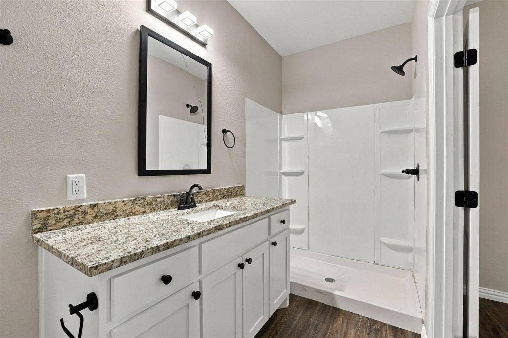 1116 S 6th Avenue, Denison, TX 75021 Bathroom featuring a white vanity cabinet, patterned stone countertop with an integrated sink, matte black faucet and hardware, framed mirror, and a walk-in shower surround
