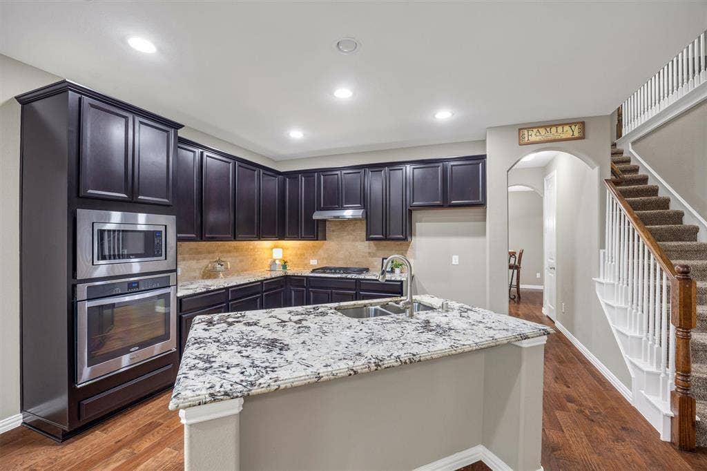 3014 Aurora Mist Drive, Little Elm, TX 75068 Kitchen featuring dark cabinetry, stone countertops, stainless steel double wall ovens, a central island with a double-basin sink, and recessed lighting