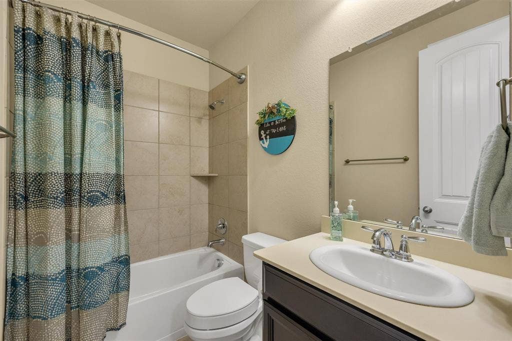 3014 Aurora Mist Drive, Little Elm, TX 75068 Bathroom featuring a dark-finish vanity with a light-toned countertop, a drop-in porcelain sink, a full-width vanity mirror, and a tub-shower combination with tile surround