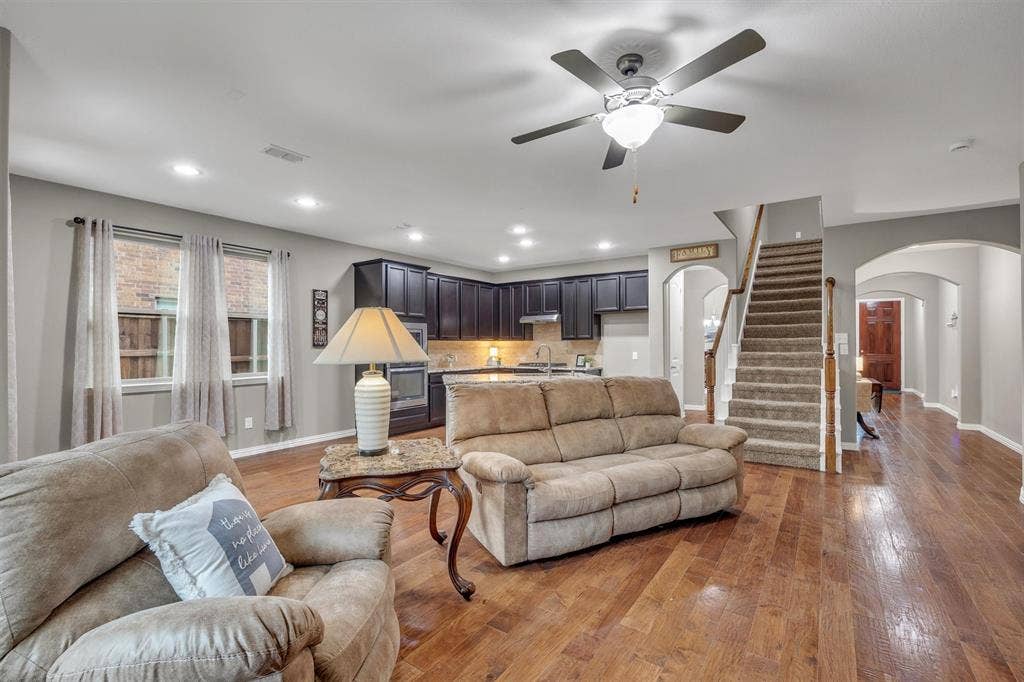 3014 Aurora Mist Drive, Little Elm, TX 75068 Open-concept interior featuring wood-finish flooring, recessed lighting, dark cabinetry with stone countertops, a ceiling fan with integrated lighting, and a staircase with a wooden handrail