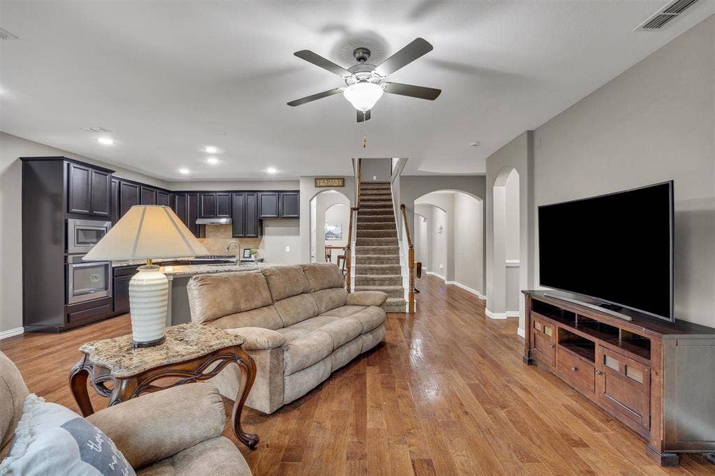 3014 Aurora Mist Drive, Little Elm, TX 75068 Open-concept interior featuring dark-toned built-in cabinetry, recessed lighting, wood-finish flooring, a kitchen island with stone-finish countertops, and an arched entryway