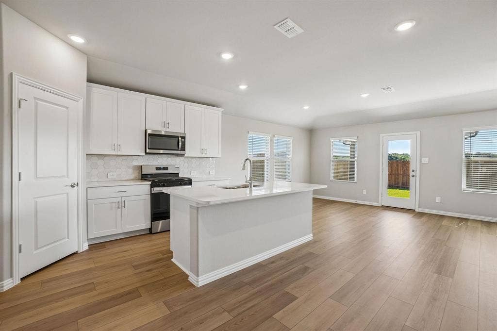 6110 CHICKNEY Drive, Princeton, TX 75071 Kitchen featuring white shaker-style cabinetry, a central island with a solid surface countertop, stainless steel appliances, geometric tile backsplash, and wood-finish flooring