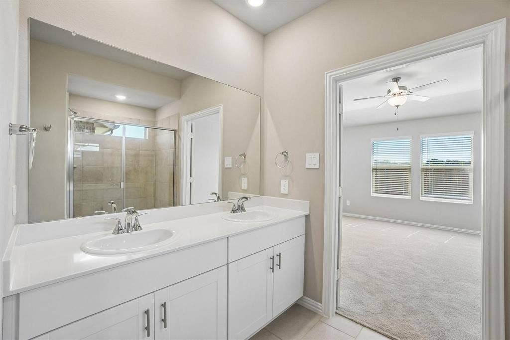 6110 CHICKNEY Drive, Princeton, TX 75071 Dual-sink vanity with white cabinetry and solid-surface countertop, full-width mirror, and a glass-enclosed shower with tile surround