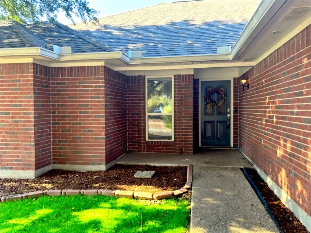 Traditional red brick exterior featuring an arched-top front door with glass inlay, concrete entryway, and mulched landscaping beds