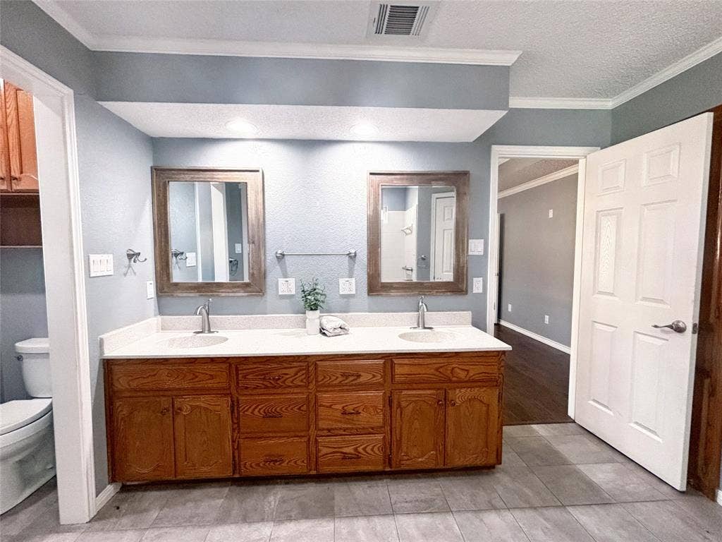 Dual-sink vanity with solid-surface countertop, wood cabinetry, two framed mirrors, and tile flooring