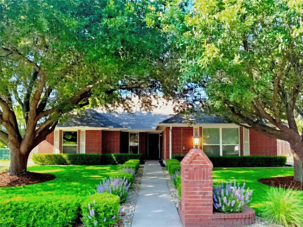 Brick exterior residence featuring a front walkway, mature trees, manicured hedges, and a brick pillar entryway